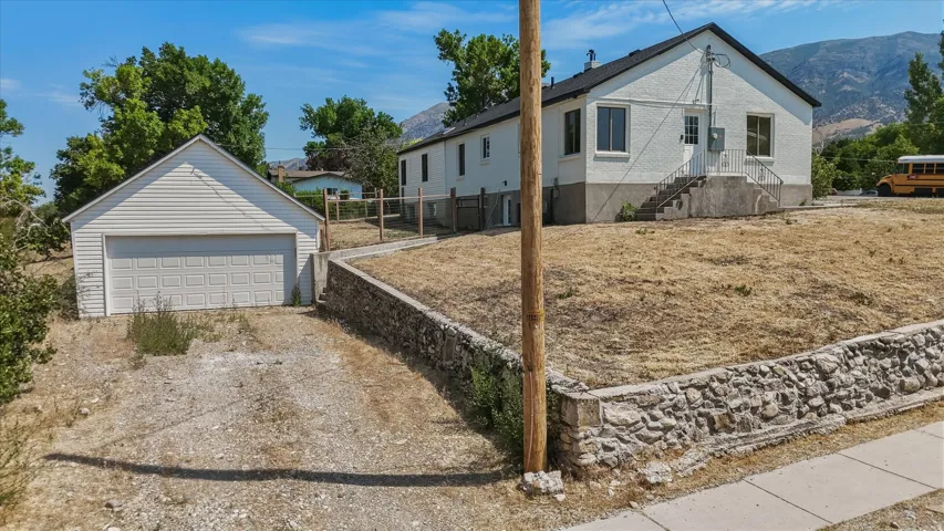 White exterior residence featuring a detached garage, terraced landscaping with a stone retaining wall, and a concrete pathway