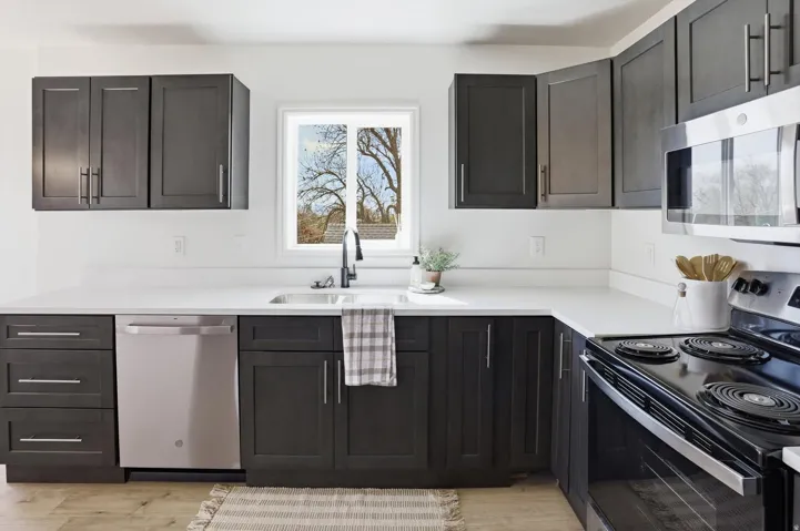 Kitchen featuring dark wood-finish cabinetry, white countertops, stainless steel appliances, and a window above the sink