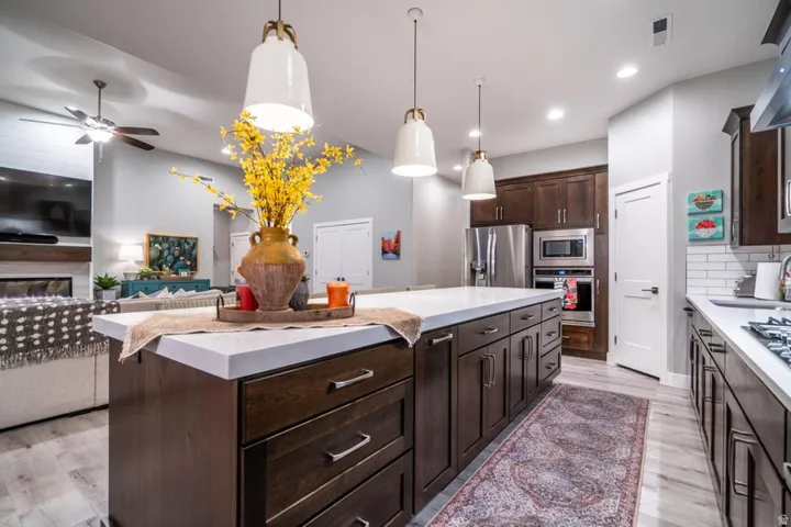 Kitchen with dark wood finish cabinets, stainless steel appliances, open floor plan, hanging light fixtures, and light wood-type flooring