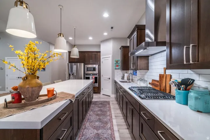 Kitchen featuring dark wood finish cabinets, stainless steel appliances, backsplash, light stone countertops, and light wood finished floors
