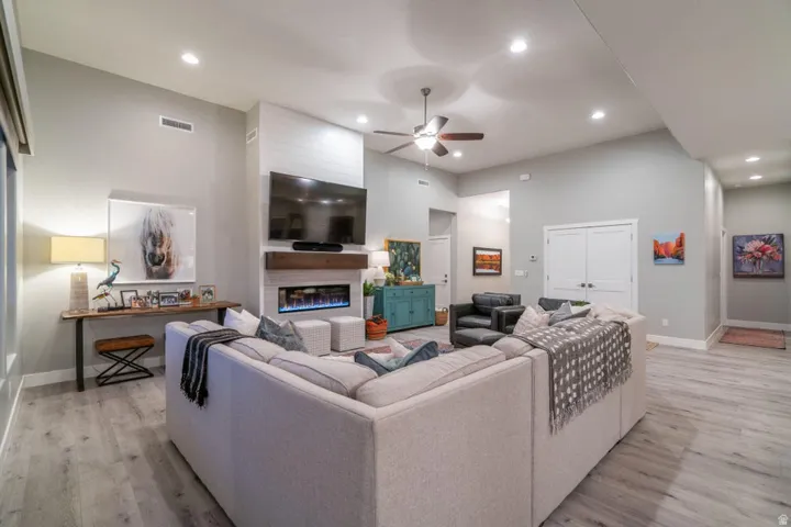 Living room with ceiling fan, a glass covered fireplace, a high ceiling, light wood-style flooring, and recessed lighting