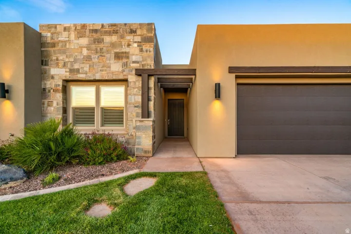 View of front of property with stone siding, an attached garage, driveway, and stucco siding