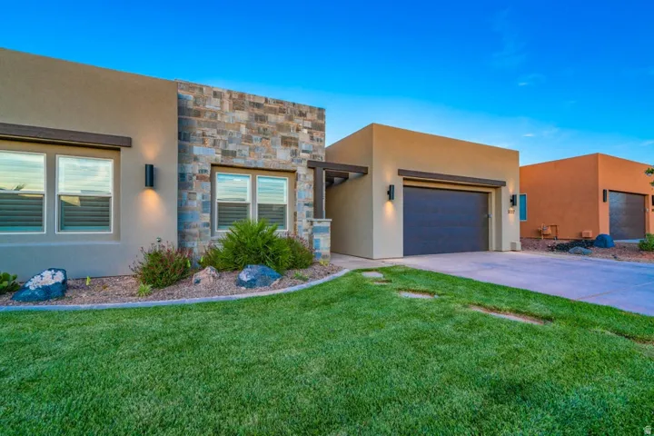 Southwest-style home with stucco siding, an attached garage, concrete driveway, a front yard, and stone siding