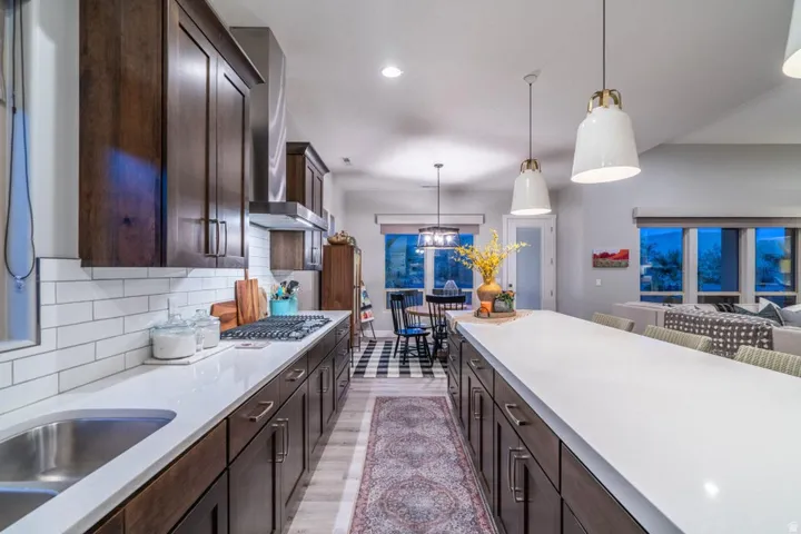 Kitchen with dark wood finish cabinets, light wood-type flooring, pendant lighting, light stone counters, and backsplash