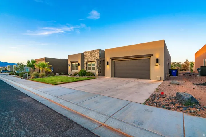 Adobe home with an attached garage, stone siding, stucco siding, and concrete driveway