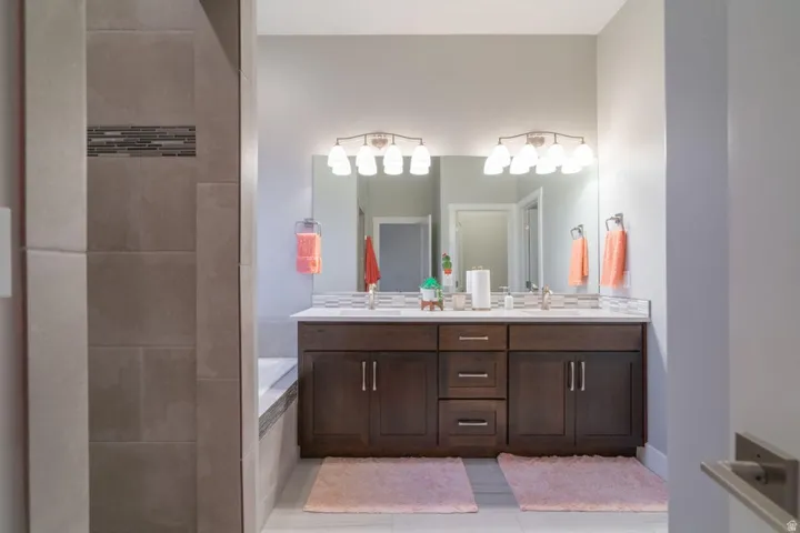 Full bath with double vanity, light tile patterned floors, a garden tub, and tiled shower