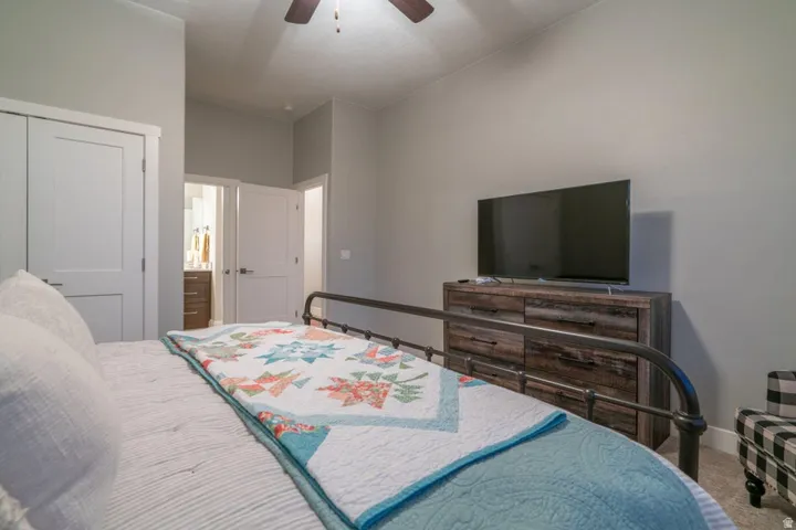 Carpeted bedroom featuring a closet, ensuite bathroom, and a ceiling fan