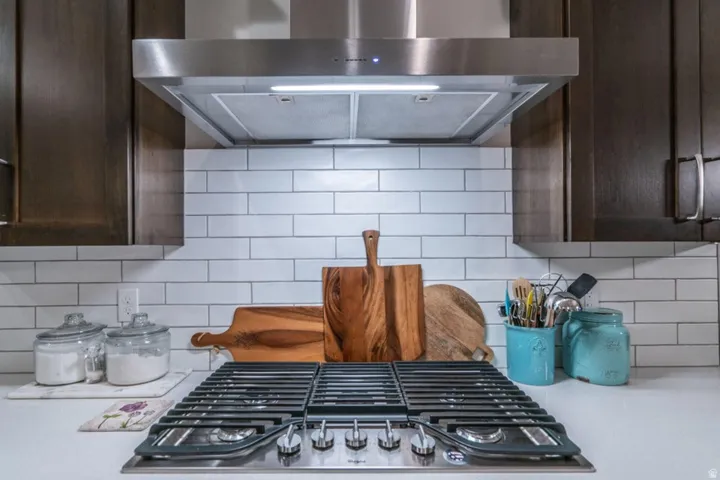 Kitchen view of extractor fan, dark wood finish cabinets, tasteful backsplash, and stainless steel gas stovetop