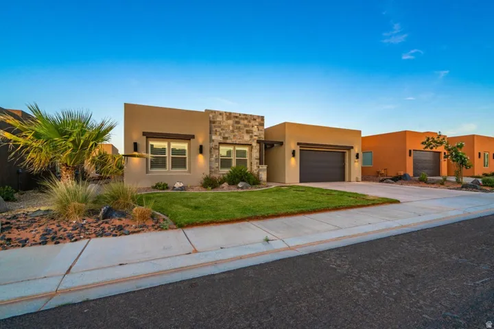 Pueblo-style house with stone siding, stucco siding, a garage, driveway, and a front lawn