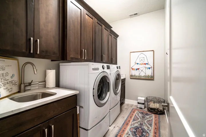 Laundry area featuring washer and clothes dryer, cabinet space, and light wood-style flooring