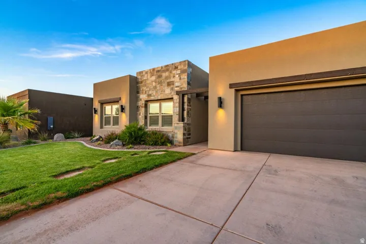 Southwest-style home with stone siding, concrete driveway, a front lawn, stucco siding, and an attached garage