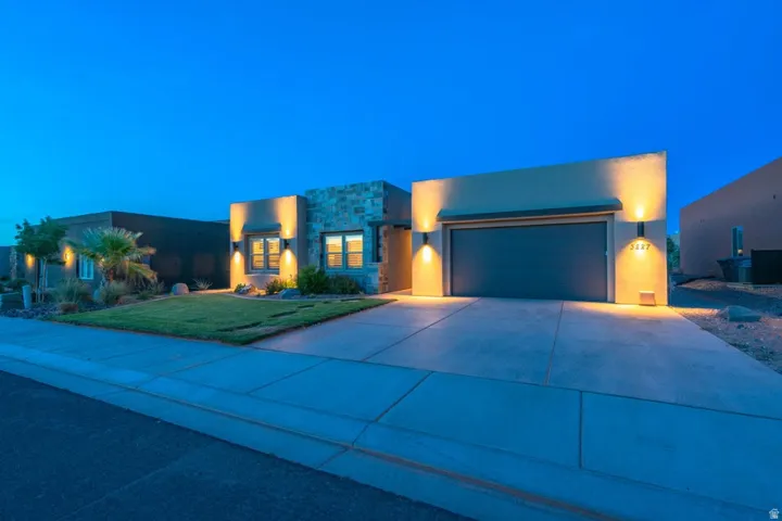 Contemporary house featuring stone siding, stucco siding, concrete driveway, a garage, and a front lawn