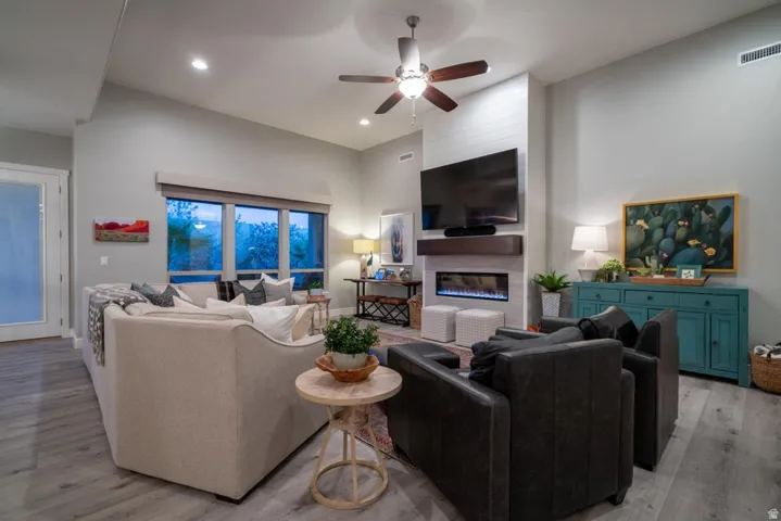 Living area featuring a ceiling fan, light wood finished floors, a glass covered fireplace, a high ceiling, and recessed lighting