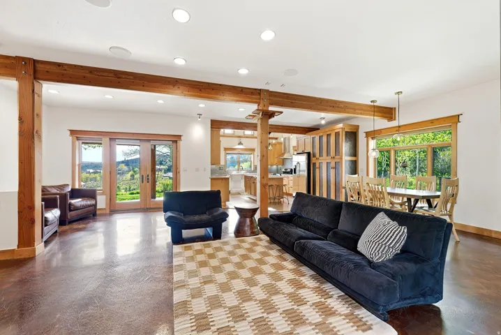 Open-concept living space featuring wood-finish flooring, exposed timber beams, recessed lighting, and large glass French doors