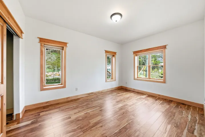 Expansive room featuring wood-finish flooring, white walls, and three windows with natural wood trim
