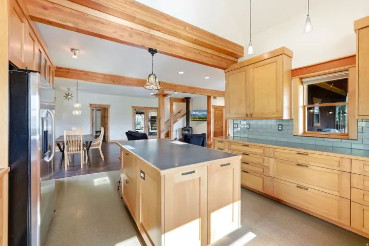 Kitchen featuring light wood cabinetry, a large central island with a solid surface countertop, stainless steel refrigerator, and a light blue tile backsplash