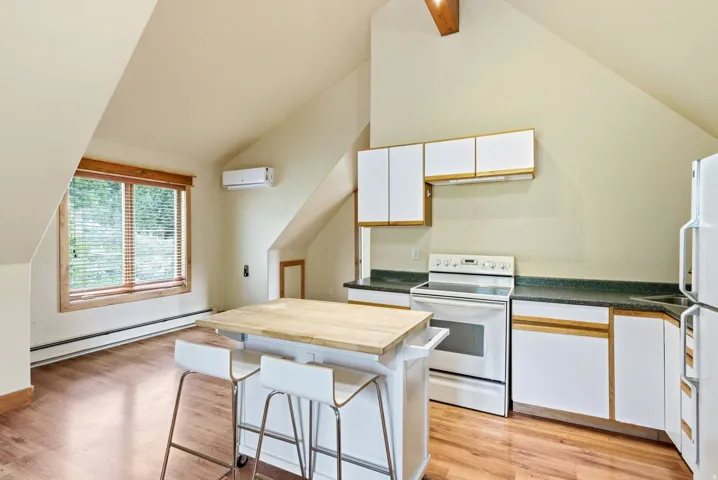 Compact kitchen area featuring white appliances, white cabinetry with wood-finish trim, and dark countertops