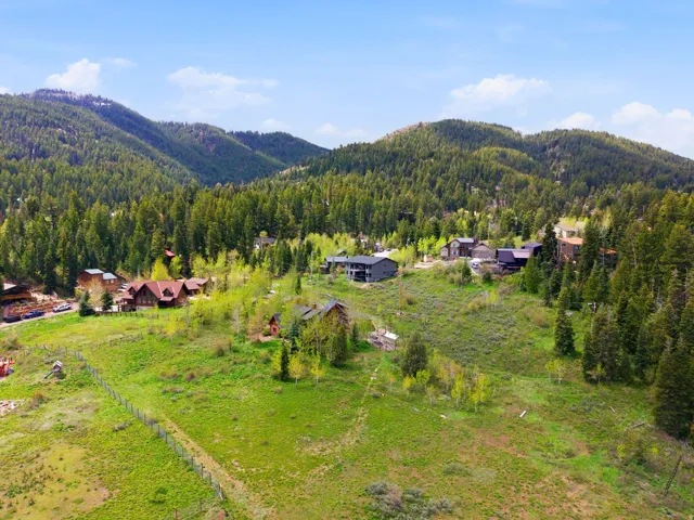Expansive mountain landscape featuring dense evergreen and deciduous trees, with multiple properties nestled on undulating terrain