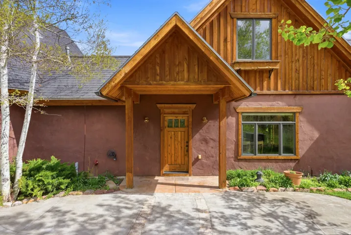 Entryway featuring a wood-panel door with glass inserts, covered porch with natural wood beams, and complementary exterior lighting