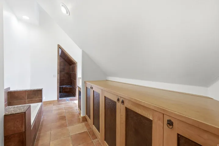 Built-in cabinetry with wood-finish doors and metal inserts, ceramic tile flooring, built-in bathtub with tiled surround, and a tiled shower stall with a built-in bench
