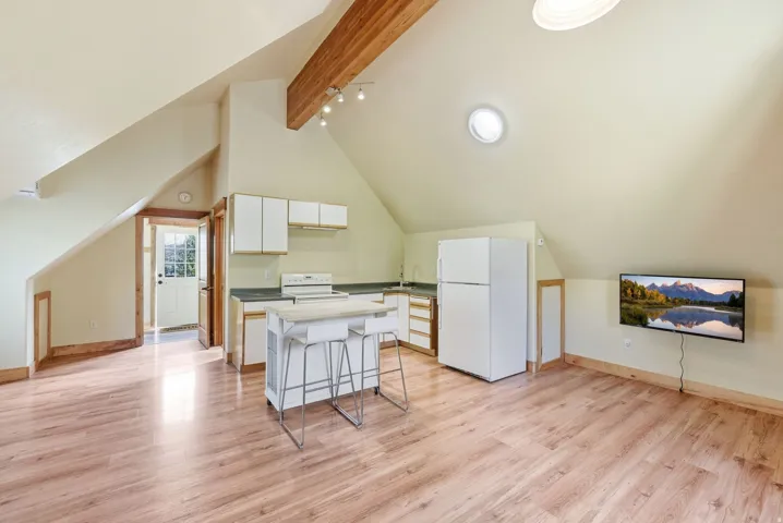 Open-concept living space featuring wood-finish flooring, a kitchen area with white cabinetry and a white refrigerator, and an exposed wood beam