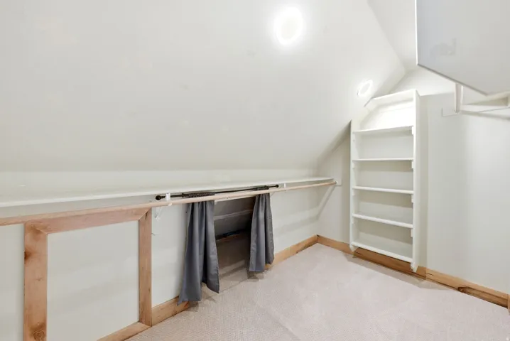 Attic space featuring sloped ceilings, recessed lighting, built-in shelving, a clothes hanging rod, and carpet flooring