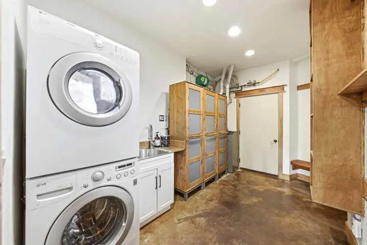 Laundry room with stacked washer and dryer, utility sink with white cabinetry, and wood-finish flooring
