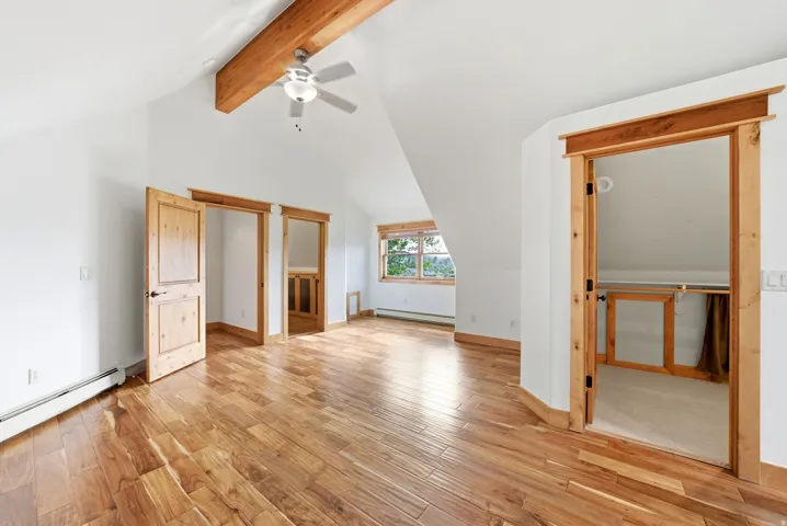 Spacious interior with vaulted ceilings, exposed wood beam, wood-finish flooring, and natural wood trim throughout