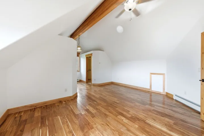 Spacious room featuring wood-finish flooring, exposed wooden beams, and a ceiling fan