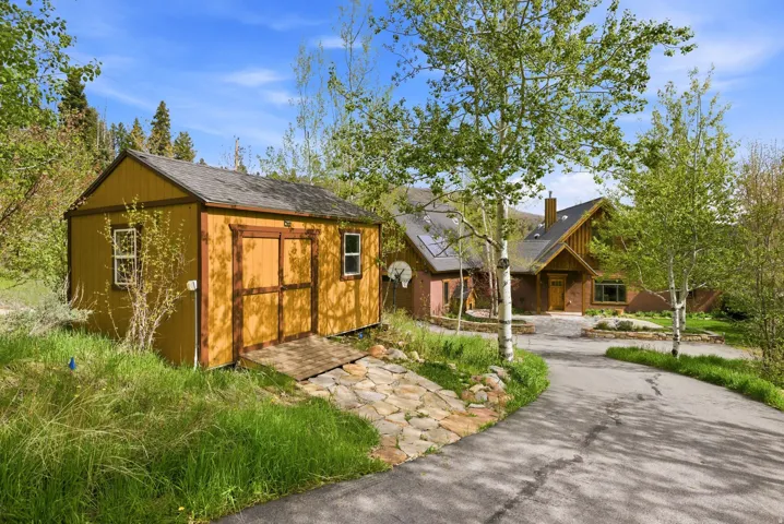 Wood-sided storage shed with a shingled roof, double entry doors, and two windows