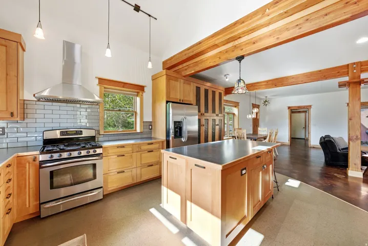 Open-concept kitchen featuring natural wood cabinetry, stainless steel appliances, a center island with a solid surface countertop, and exposed wood beams
