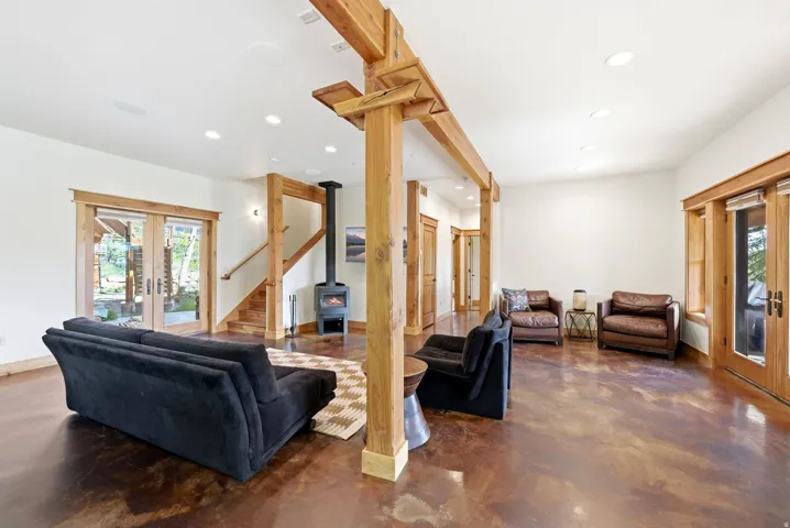 Spacious common area featuring wood-finish flooring, exposed timber beams, a freestanding wood-burning stove, recessed lighting, and dual glass French doors