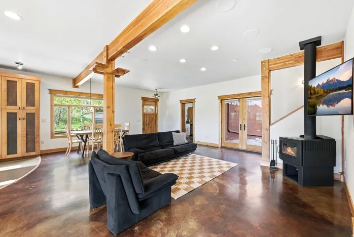 Spacious living area featuring exposed wood beams, stained concrete flooring, a freestanding wood-burning stove, and recessed lighting