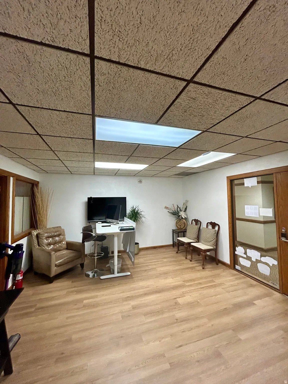 Spacious room featuring wood-finish flooring, white walls, and a suspended acoustic tile ceiling with integrated lighting