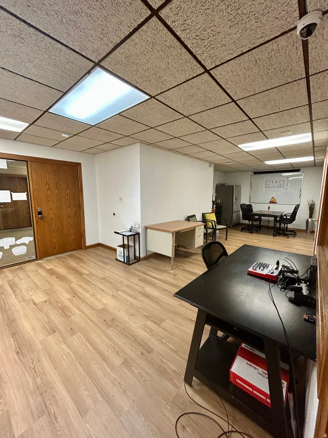 Spacious room featuring wood-finish flooring, drop ceiling with recessed lighting, and a light wood-finish door