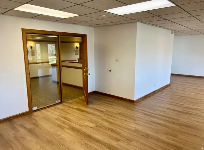 Open interior space featuring wood-finish flooring, white walls, and a suspended ceiling with recessed lighting