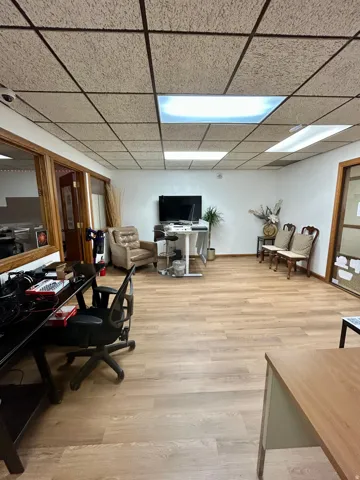 Spacious interior featuring wood-finish flooring, a drop ceiling with integrated fluorescent lighting, and natural wood door frames