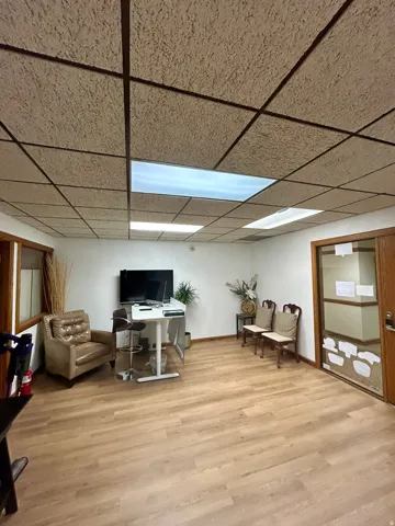 Spacious room featuring wood-finish flooring, white walls, and a suspended acoustic tile ceiling with integrated lighting