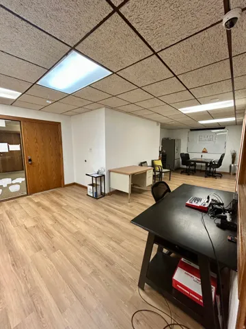 Spacious room featuring wood-finish flooring, drop ceiling with recessed lighting, and a light wood-finish door