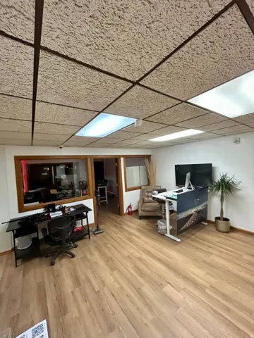 Spacious room featuring wood-finish flooring, drop ceiling with integrated lighting, and a windowed partition