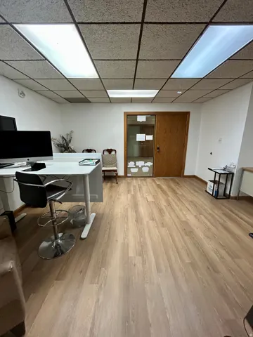 Spacious room featuring wood-finish flooring, white walls, and a drop ceiling with integrated rectangular lighting