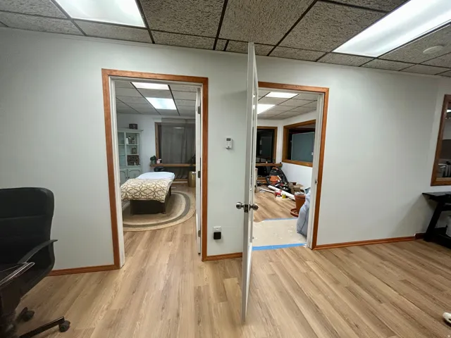 Interior space featuring wood-finish flooring throughout, two entryways with wood trim, white walls, and a suspended acoustic tile ceiling with integrated lighting