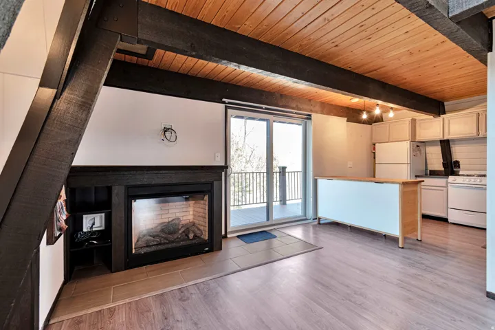 Interior featuring exposed dark wood beams, natural wood ceiling, wood-finish flooring, and a fireplace with a black mantel