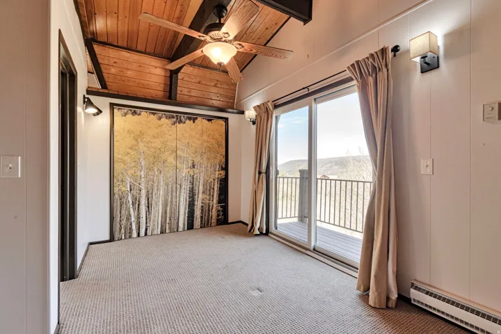 Room featuring a vaulted wood-plank ceiling, wood-finish ceiling fan, sliding glass door to an outdoor deck, recessed wall sconces, and neutral carpet