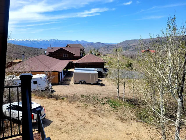 Expansive property featuring multiple structures, a gravel driveway, mature trees, and distant snow-capped mountains