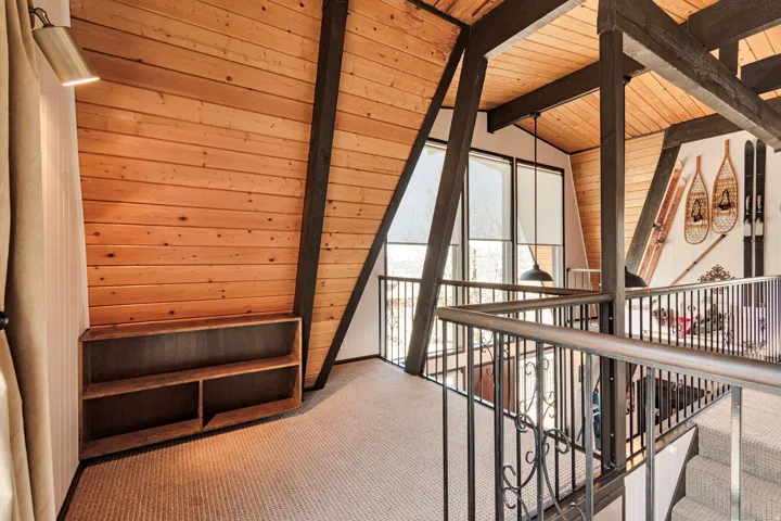 Carpeted loft space featuring an exposed wood-beam ceiling, wood-paneled walls, built-in shelving, and metal railings