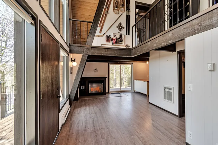 Open-concept living space with wood-finish flooring, a contemporary fireplace, and a second-story loft with wrought iron railing