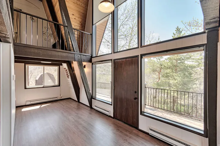 Vaulted ceiling interior with wood-finish flooring, exposed wood beams, and a second-story balcony with wrought iron railing