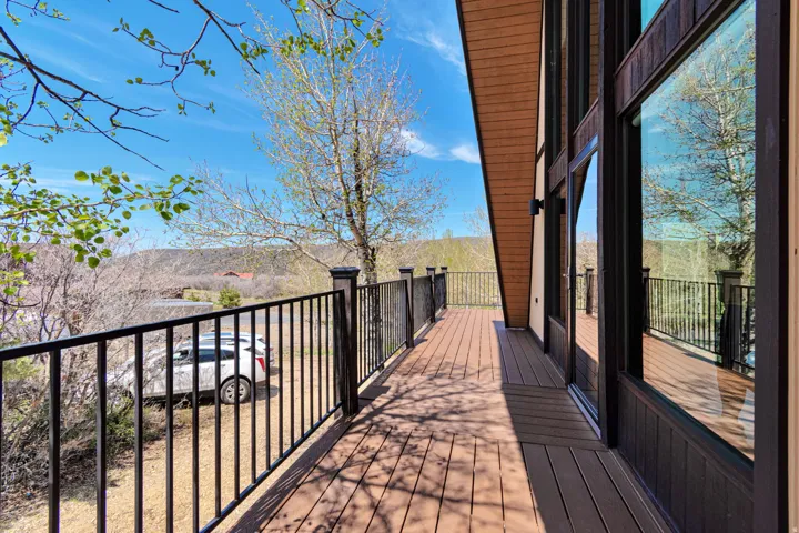 Expansive outdoor deck featuring wood-finish flooring, black wrought iron railing, and large floor-to-ceiling windows