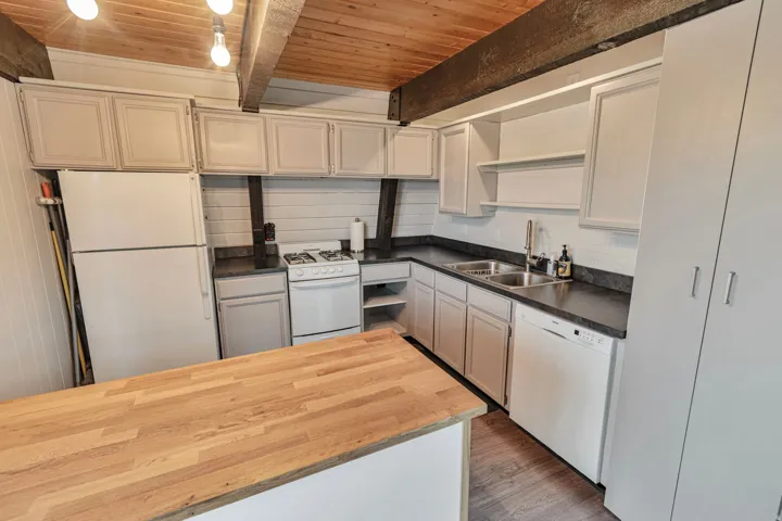 Kitchen featuring a wood-finish ceiling with exposed beams, white cabinetry, dark countertops, white subway tile backsplash, and a wood-finish island top